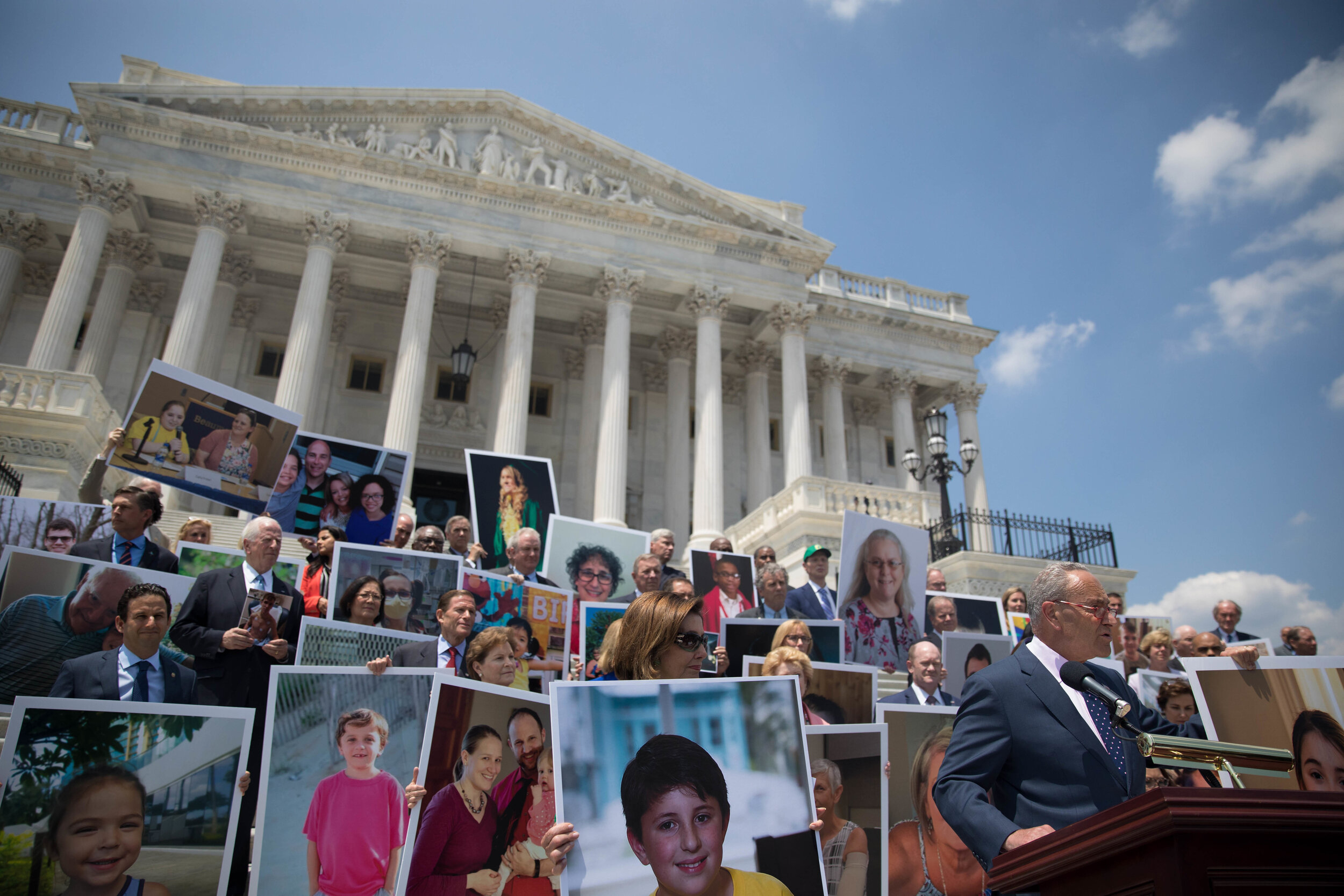Senate Democrats stand on the Supreme Court steps, holding up photos of constituents who rely on the ACA for their pre-existing conditions.